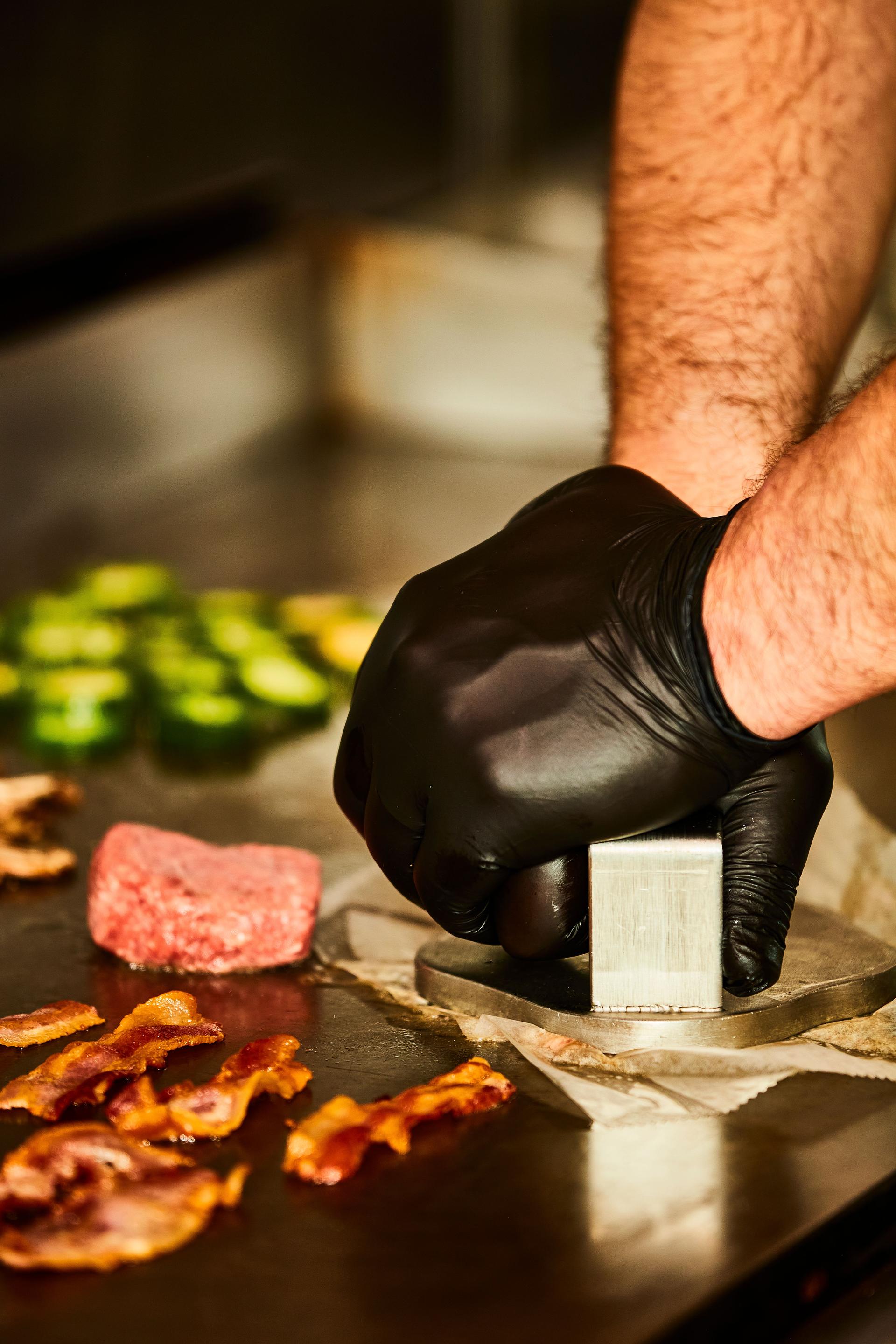 chef smashing burger on a flat top grill