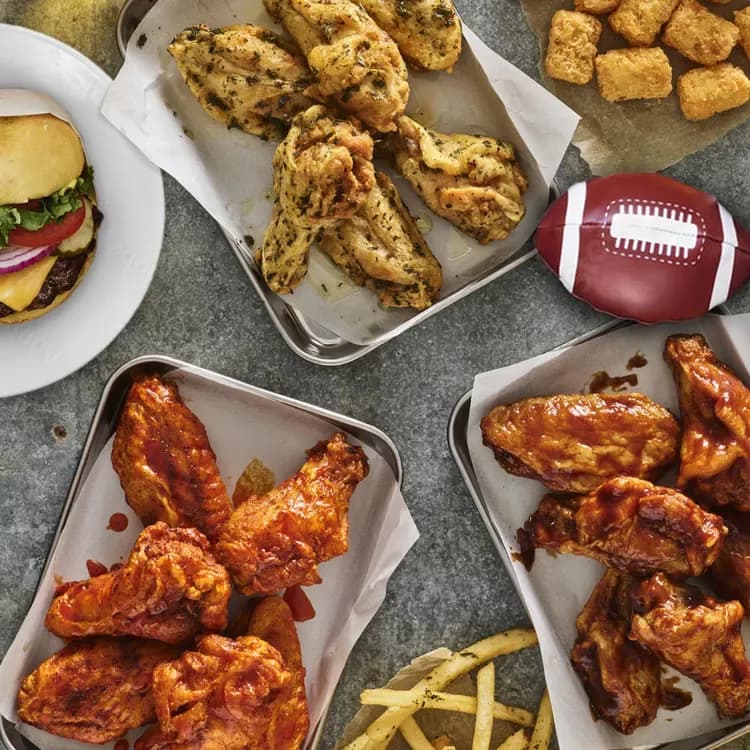 scorchin hot wings, bbq wings, and smash wings on a table with tots, a football, and a classic burger.